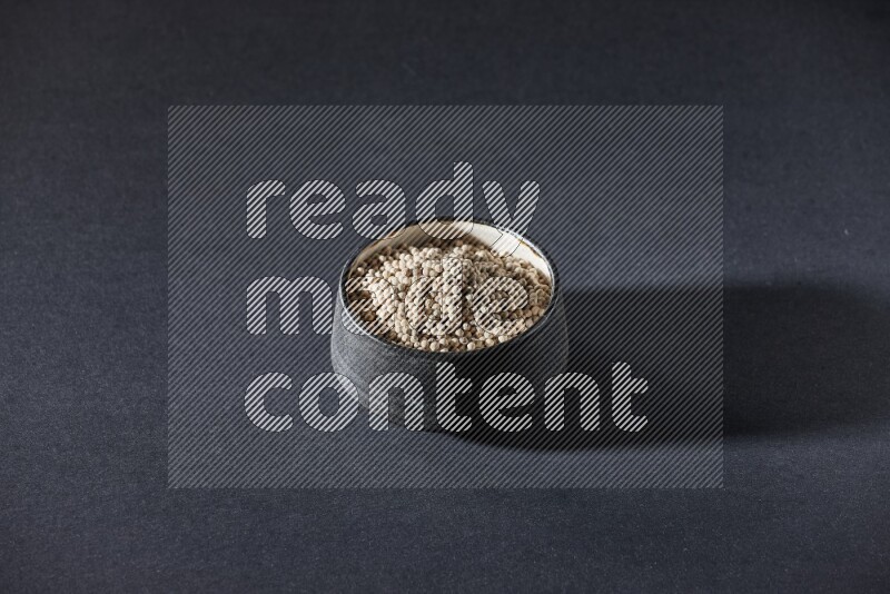 وعاء فخار أسود مملوء بالفلفل الأبيض على أرضية سوداء