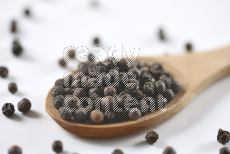 Black pepper beads with wooden spoon on white background