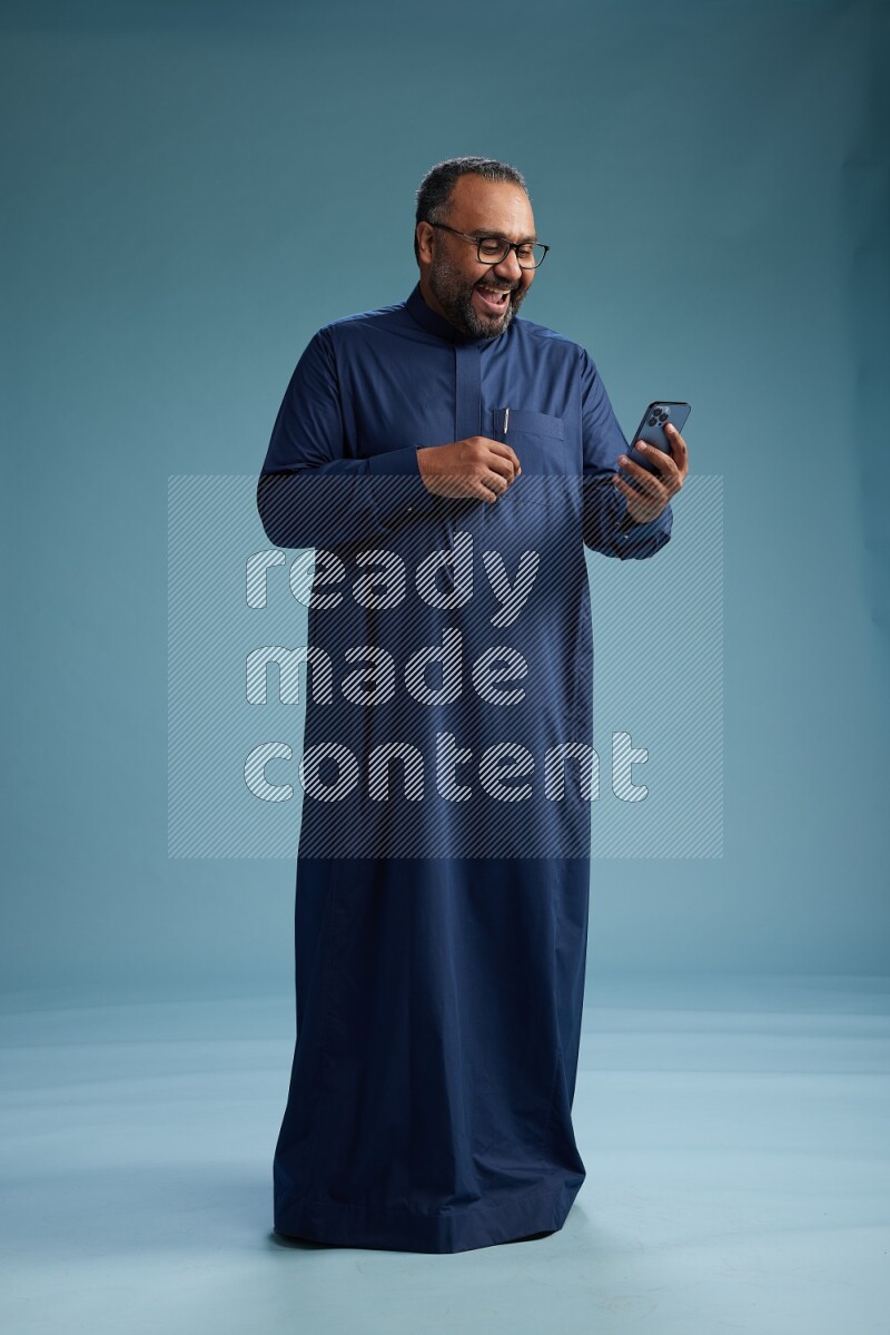 Saudi Man without shimag Standing texting on phone on blue background