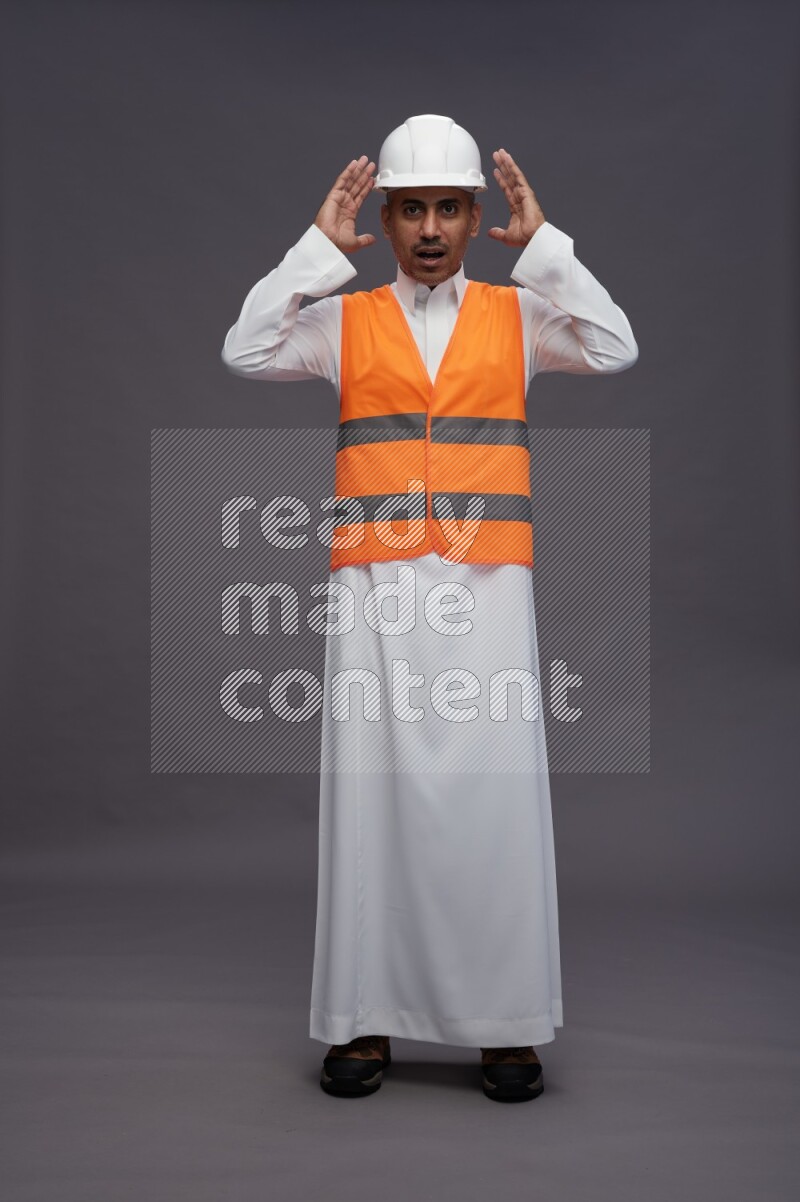 Saudi man wearing thob with engineer vest standing hands on head on gray background