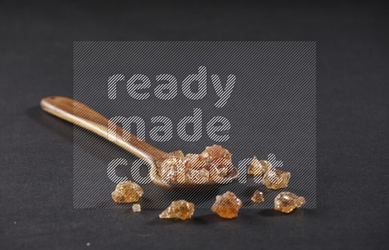 A wooden ladle filled with gum arabic on black flooring