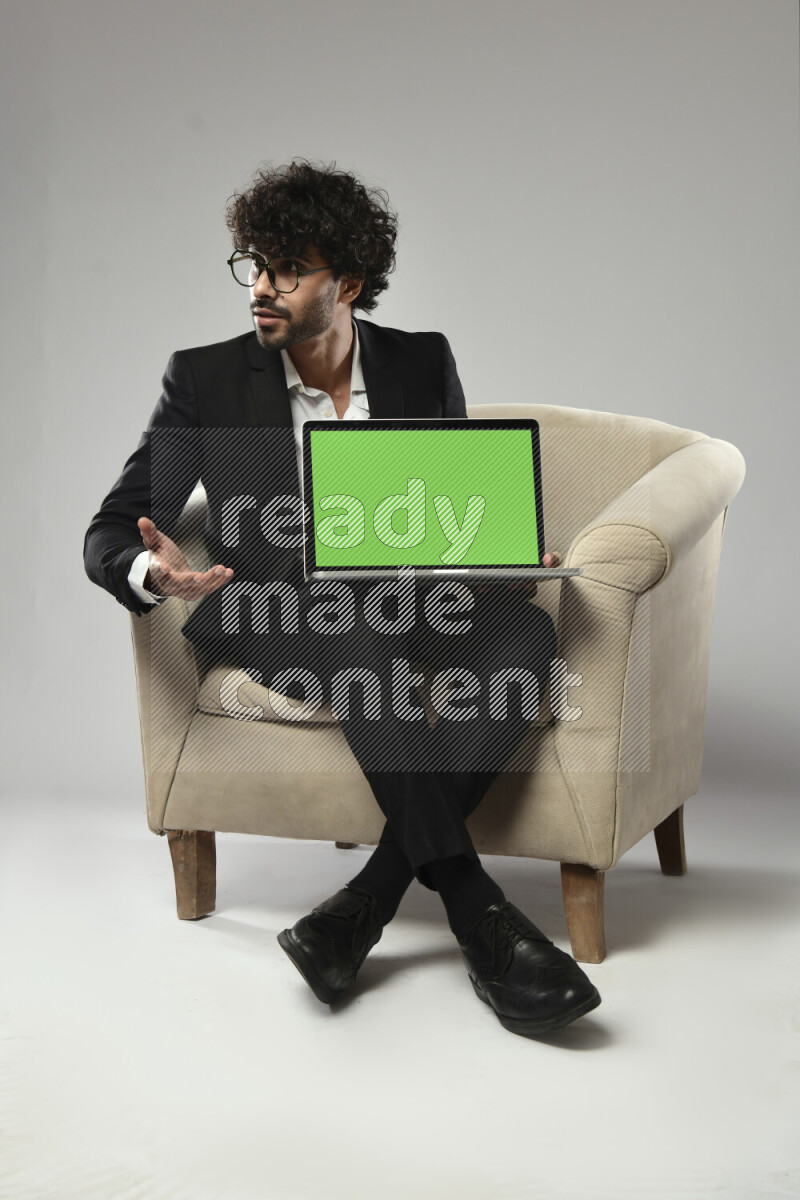 A man wearing formal sitting on a chair showing a laptop screen on white background