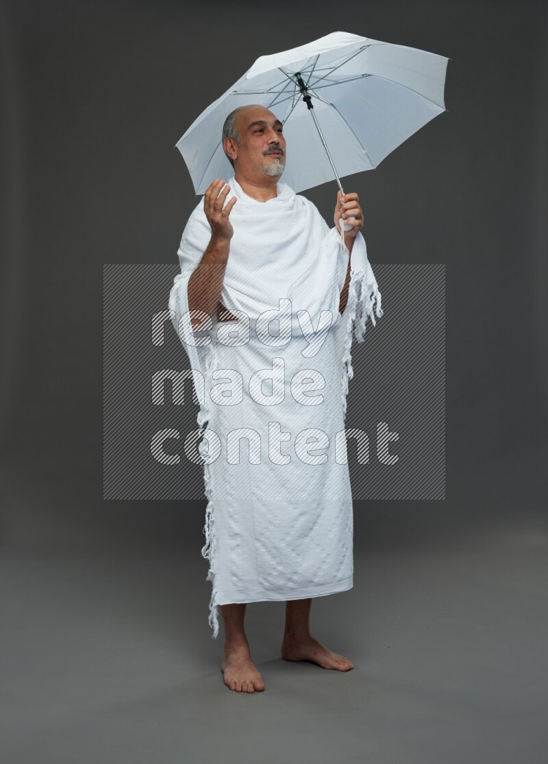 A man wearing Ehram Standing holding umbrella on gray background