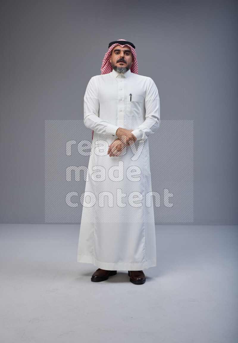 Saudi man Wearing Thob and red white Shomag standing interacting with the camera on Gray background