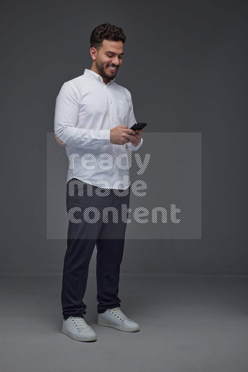 A man wearing smart casual standing and using his phone eye level on a gray background