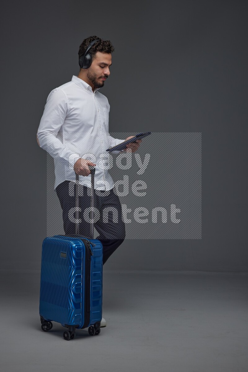 A man wearing smart casual with and pulling a carry-on luggage eye level on a gray background