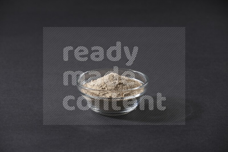 A glass bowl full of garlic powder on a black flooring