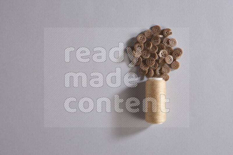 بكرة خيط خياطة بيج مع مجموعة صغيرة من الأزرار على خلفية رمادية