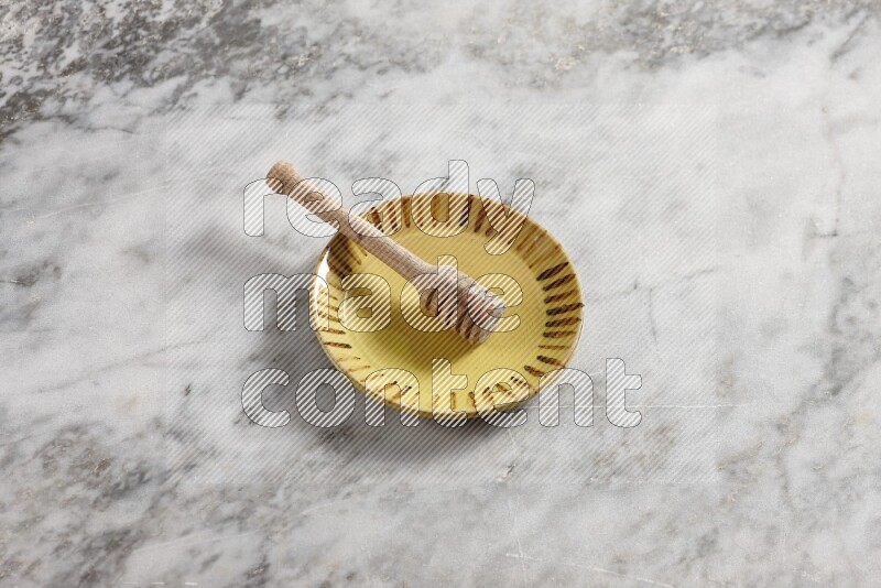 Multicolored pottery plate with wooden honey dipper in it on grey marble background