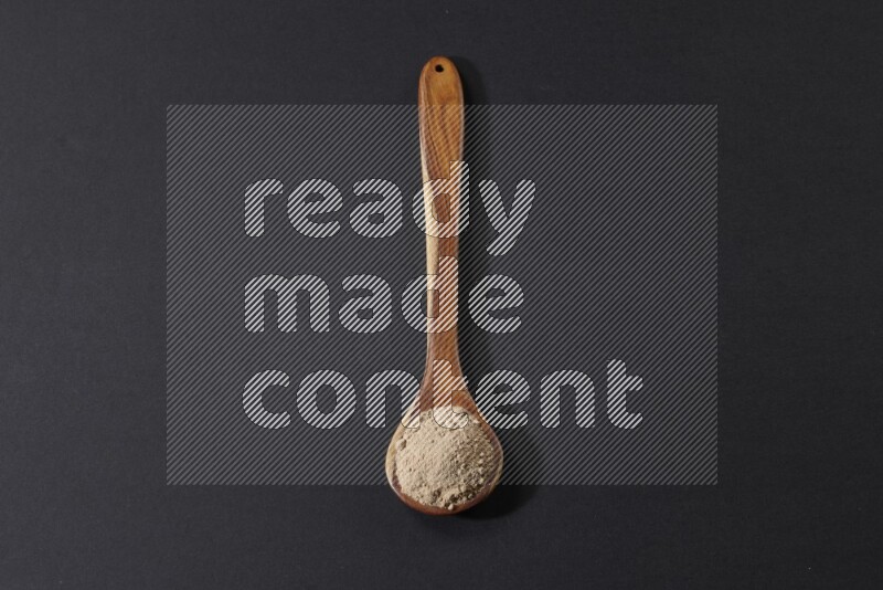 A wooden ladle full of garlic powder on a black flooring