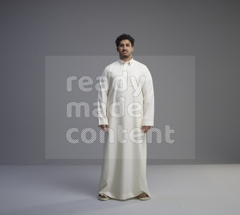 A Saudi man standing wearing thob interacting with the camera on gray background