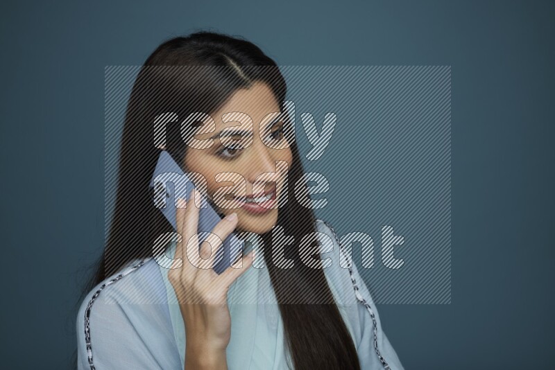 A Saudi woman having a Call in a blue background wearing a blue Abaya with no hijab