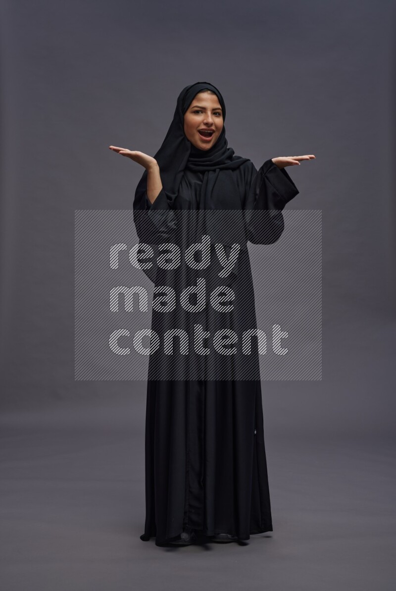 Saudi woman wearing Abaya standing interacting with the camera on gray background