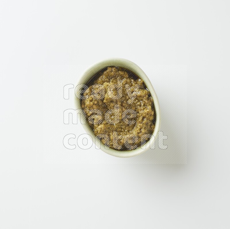 Medium oval light green ceramic bowl filled with pesto paste on a white table top