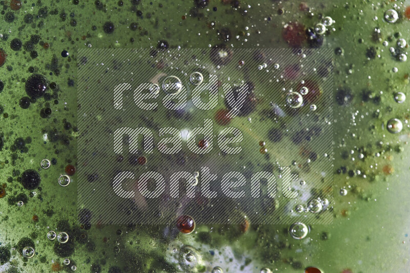 لقطات مقربة لقطرات ألوان مائية حمراء وخضراء وزرقاء على سطح الزيت على خلفية خضراء