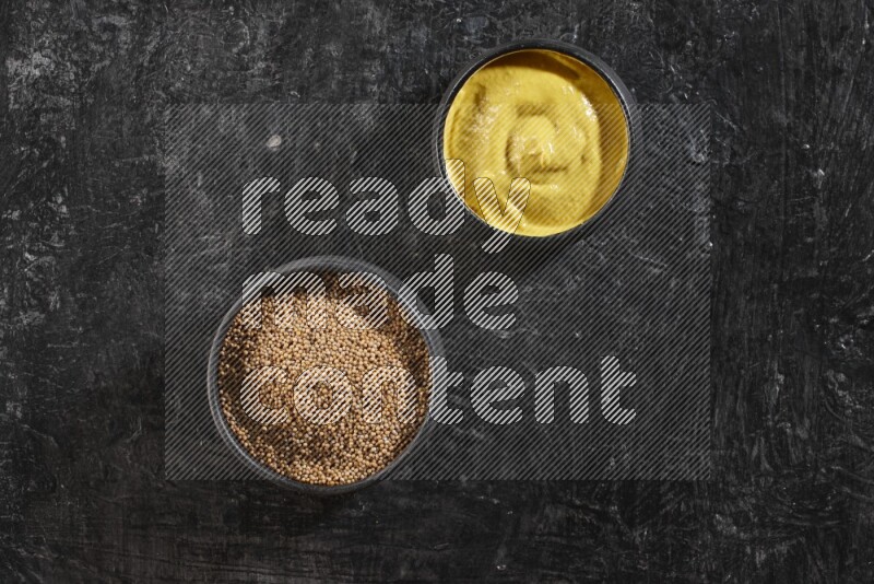 2 black pottery bowls full of mustard seeds and mustard paste on black flooring