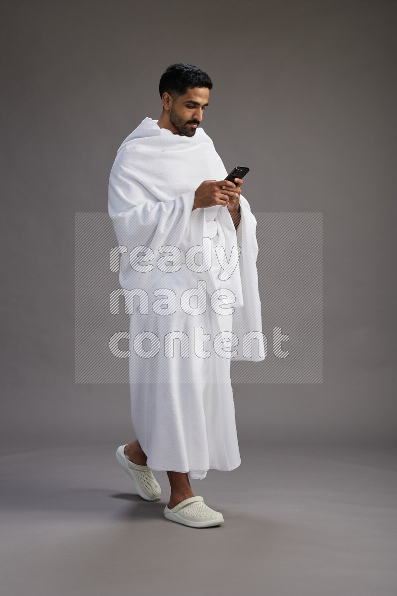 A man wearing Ehram Standing texting on phone on gray background