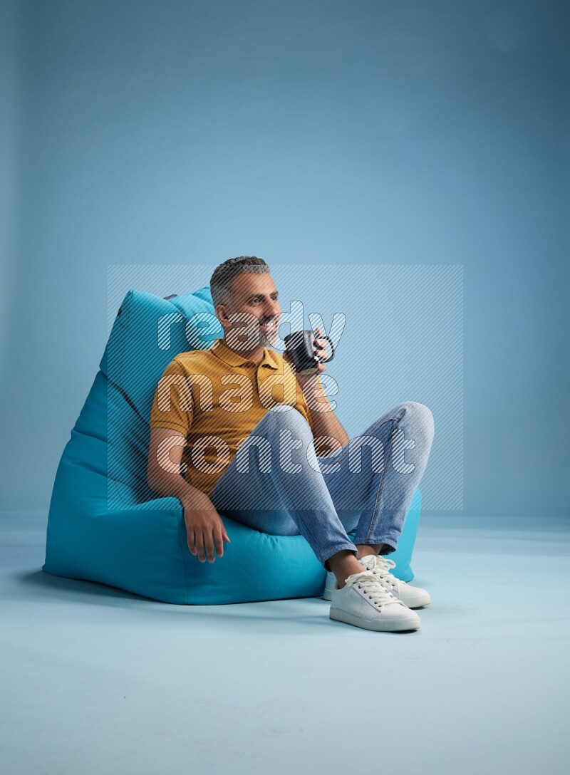 A man sitting on a blue beanbag and drinking coffee