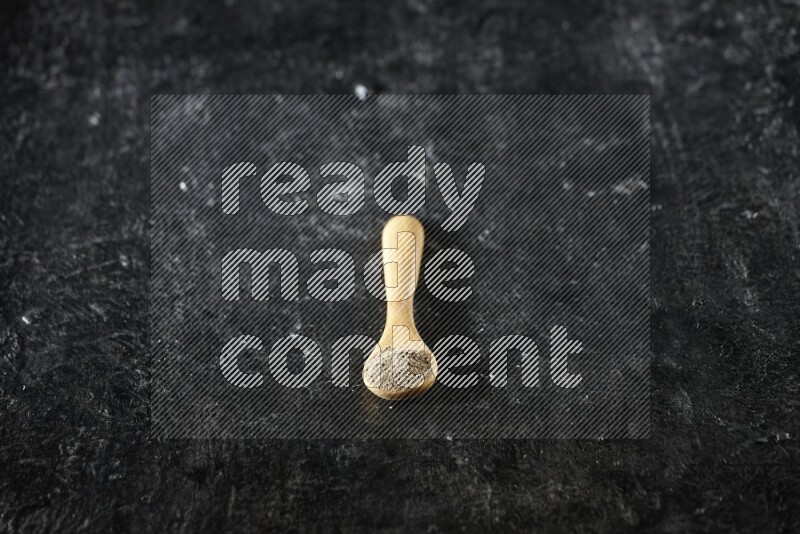 ملعقة خشبية ممتلئة ببودرة الهيل على خلفية سوداء