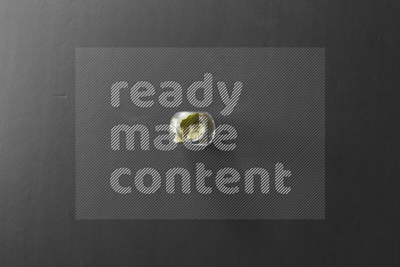 A glass spice jar full of bay laurel leaves on black flooring