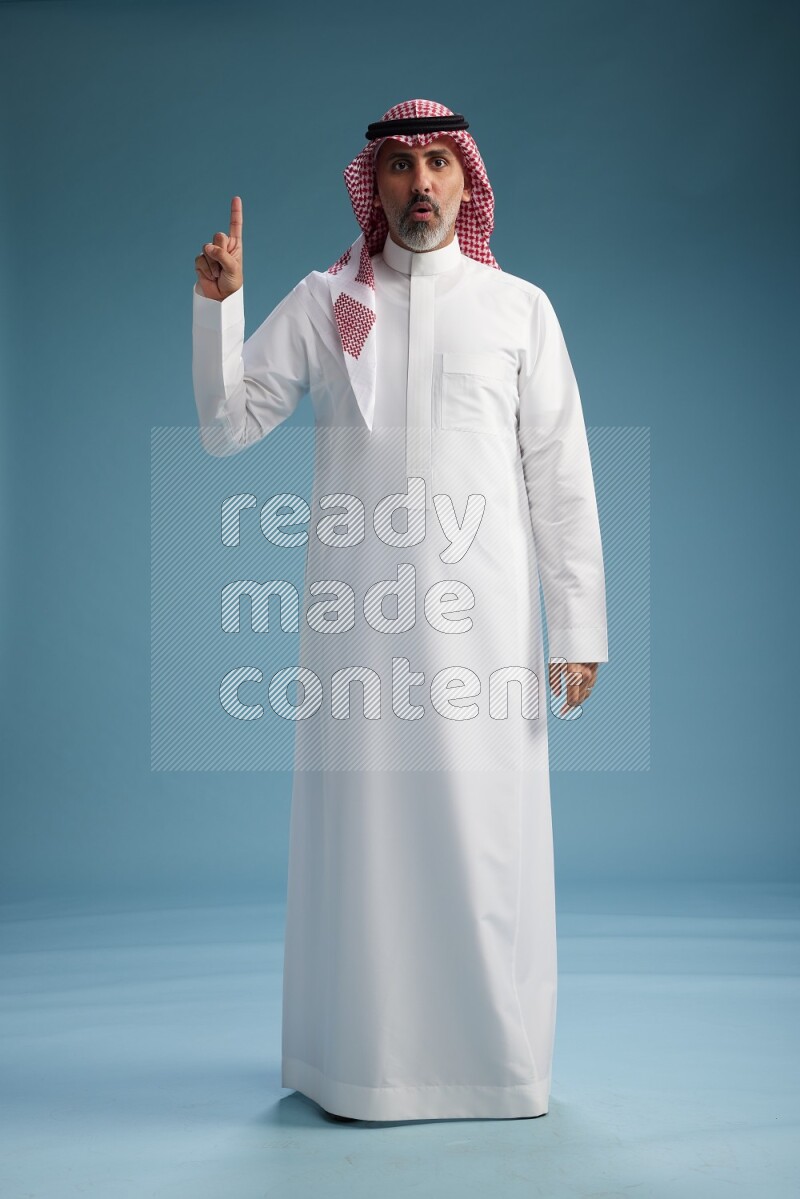 Saudi man wearing thob and shomagh posing to the camera on blue background