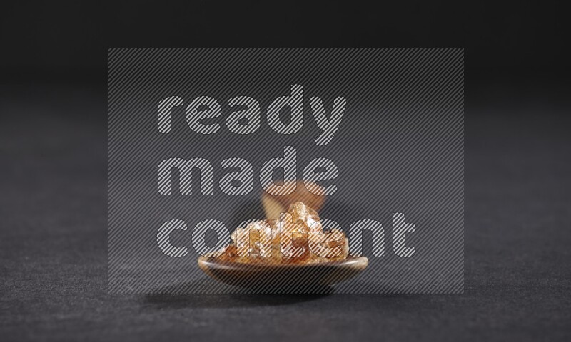 A wooden ladle filled with gum arabic on black flooring