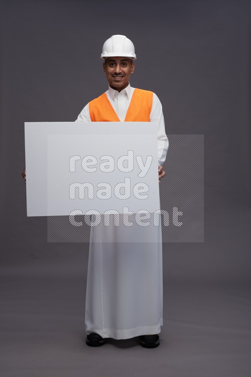 Saudi man wearing thob with engineer vest standing holding board on gray background