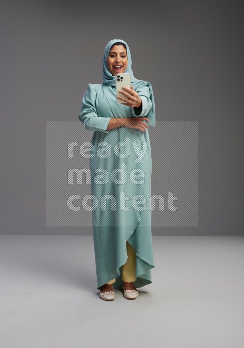 Saudi Woman wearing Abaya standing taking selfie on Gray background