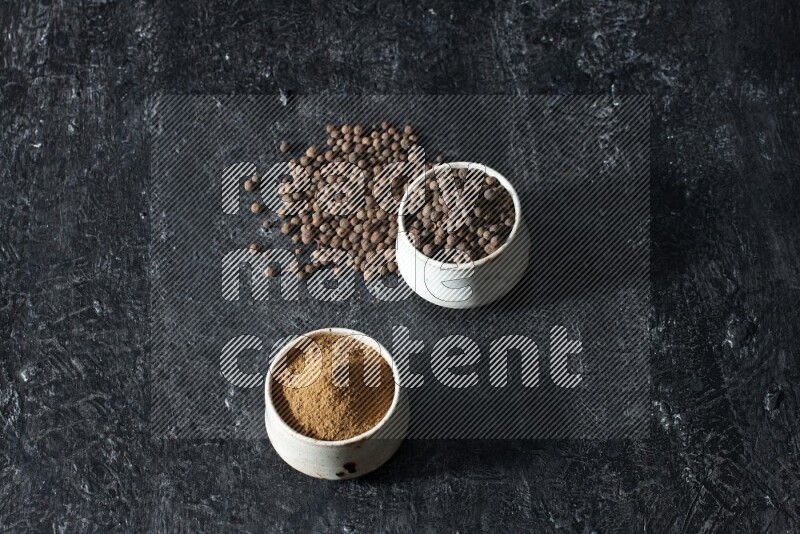 وعاءان بيج، أحدهما ممتلئ ببودرة بهار الفلفل الحلو والآخر بالحبوب وكلاهما متناثران على خلفية سوداء