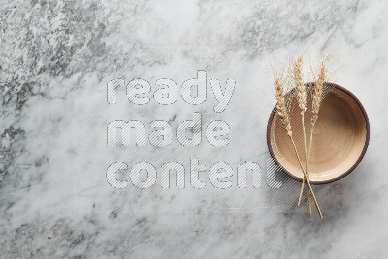 Wheat stalks on beige pottery oven bowl on grey marble background