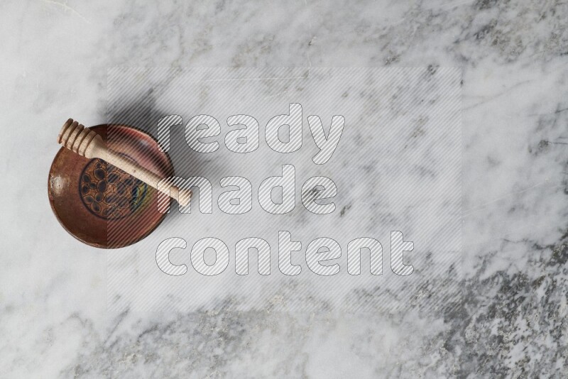 Decorative pottery plate with wooden honey dipper in it on grey marble background