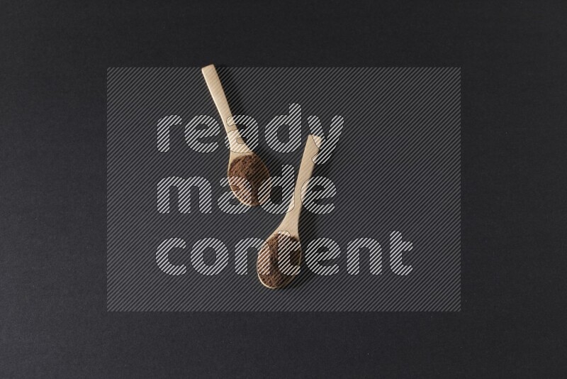 ملعقتان خشبيتان ممتلئتان ببودرة القرنفل على خلفية سوداء