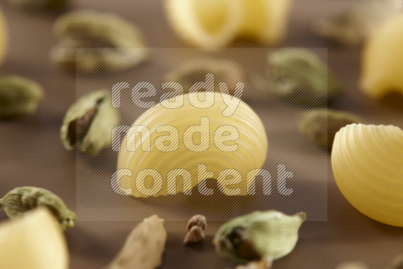 Raw pasta with different ingredients such as cherry tomatoes, garlic, onions, red chilis, black pepper, white pepper, bay laurel leaves, rosemary and cardamom on beige background