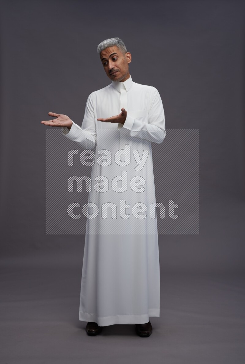 Saudi man wearing thob standing interacting with the camera on gray background