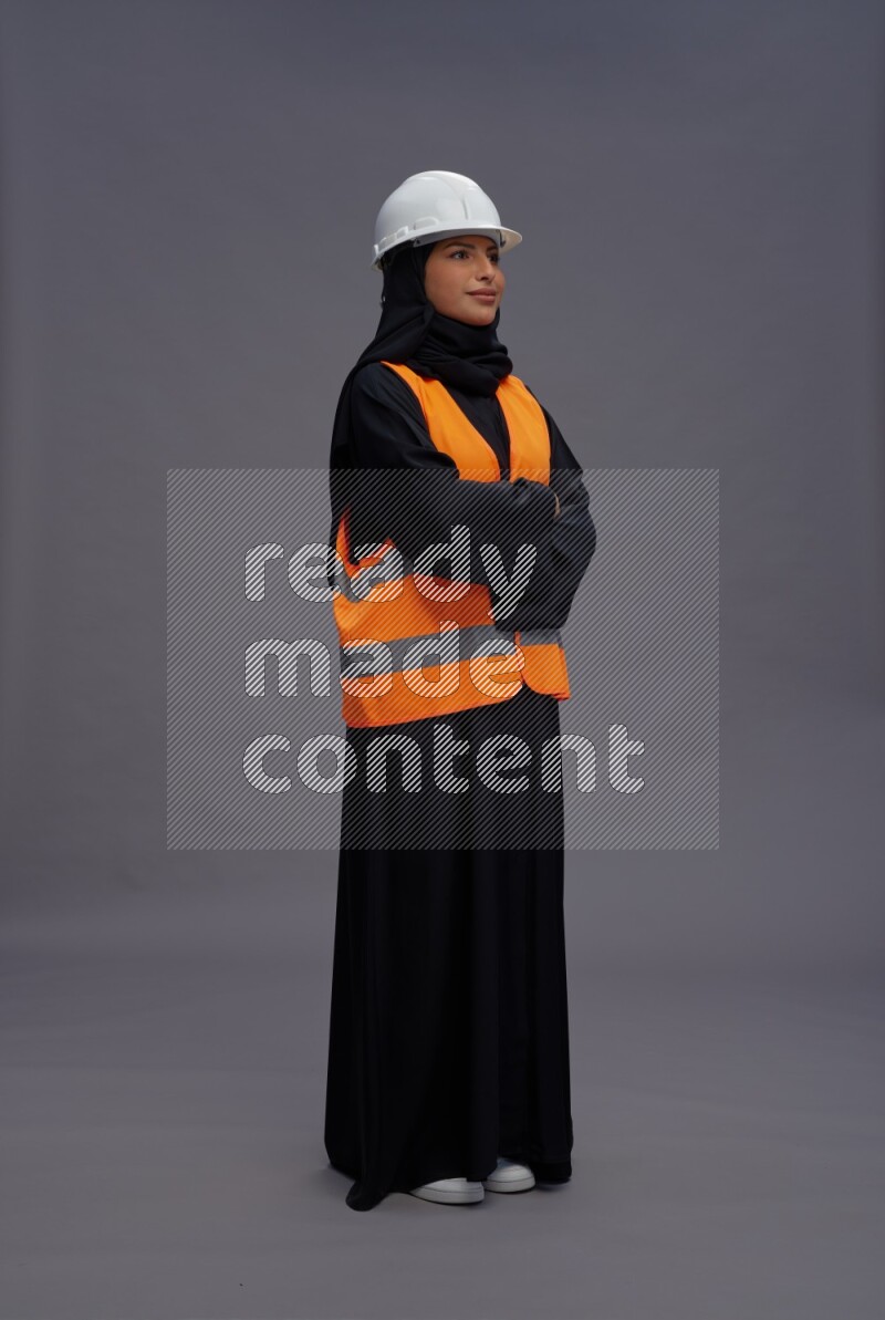 Saudi woman wearing Abaya with engineer vest standing with crossed arms on gray background