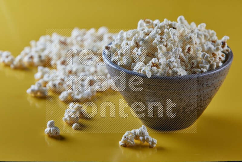 A multicolored pottery bowl full of popcorn with popcorn beside it on a yellow background in different angles