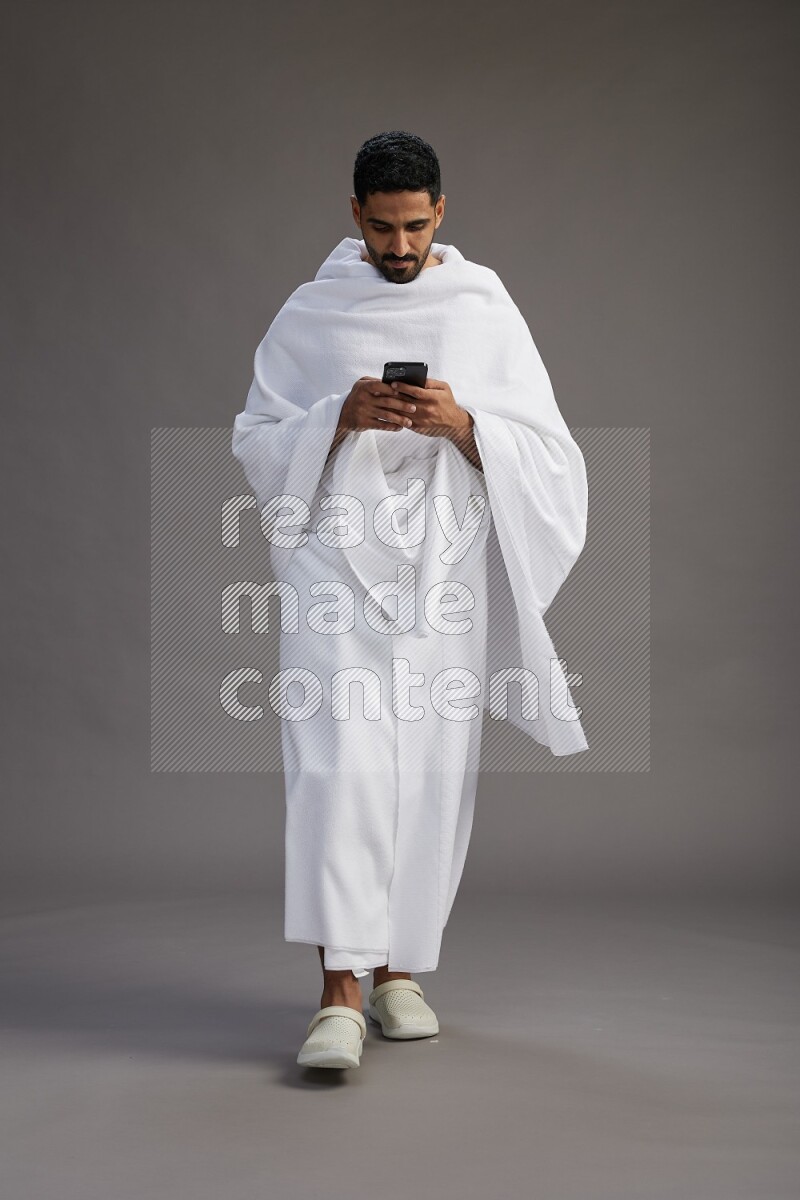 A man wearing Ehram Standing texting on phone on gray background