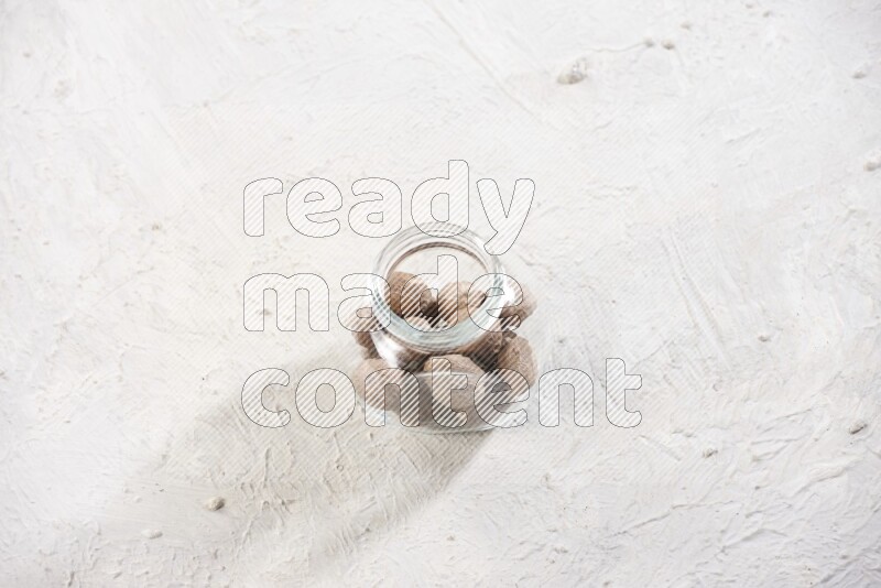 A glass spice jar full of whole nutmeg seeds on a textured white flooring