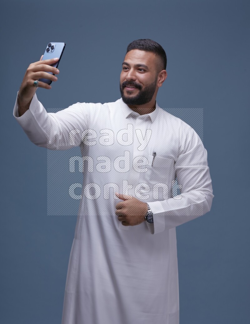 A Saudi man Taking A Selfie on Blue Background wearing Saudi Thob
