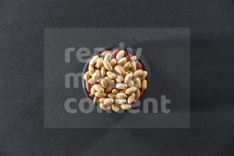 A black pottery bowl full of peeled peanuts on a black background in different angles