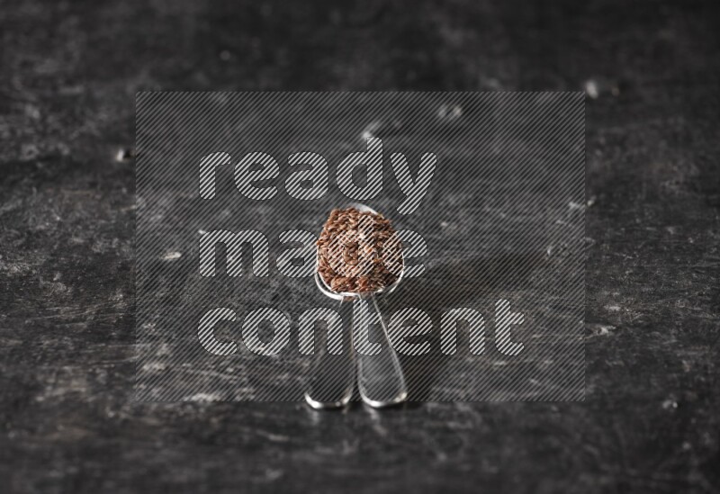 ملعقتان معدنيتان ممتلئتان بحبوب بذر الكتان علي خلفية سوداء