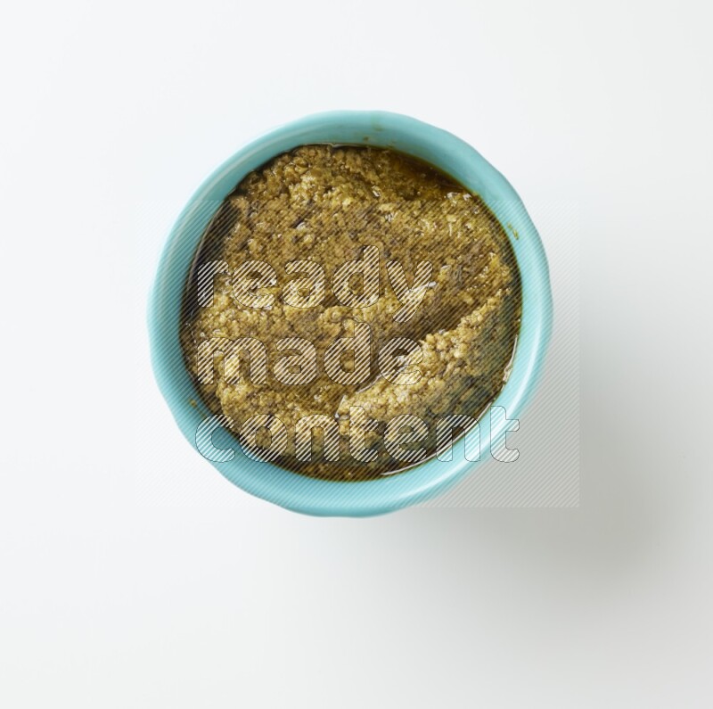 medium turquoise ceramic round bowl filled with pesto paste on a white counter top