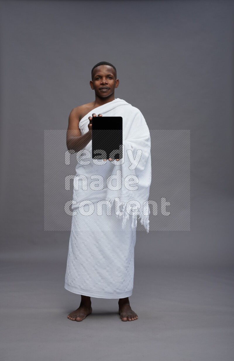 A man wearing Ehram Standing showing tablet to camera on gray background