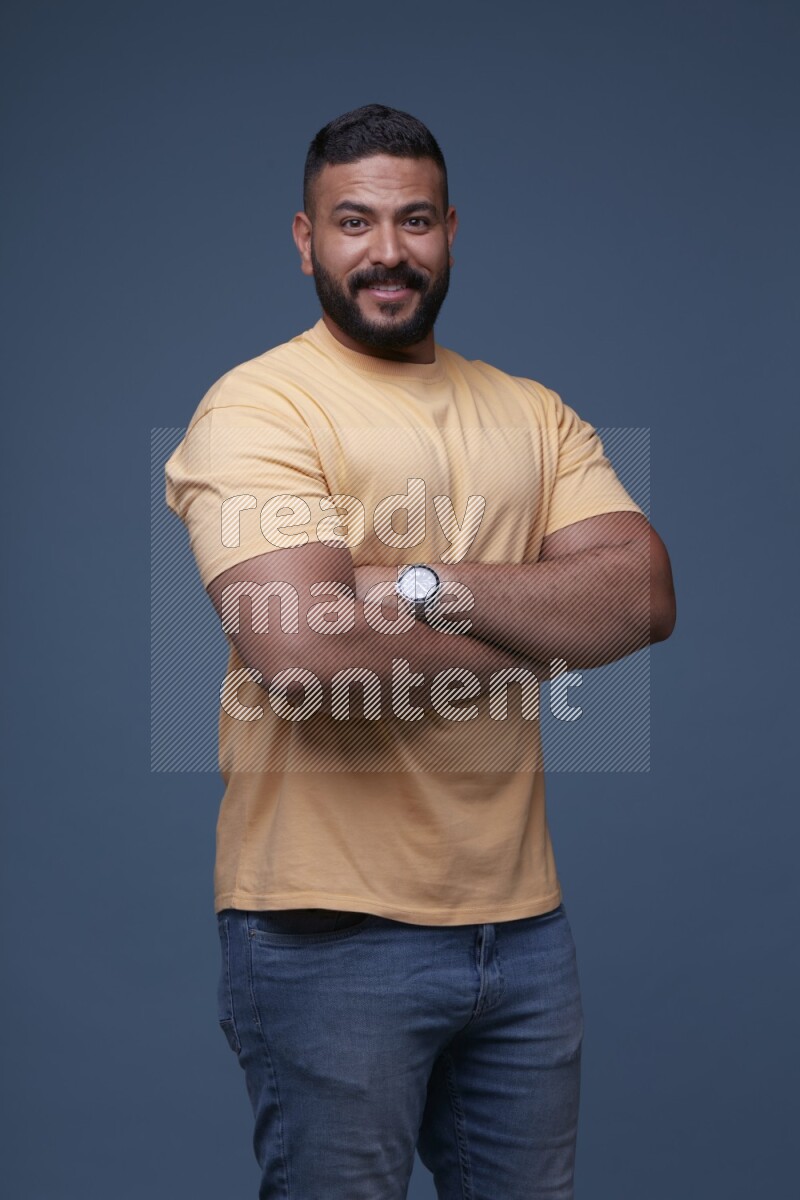A man posing in a blue background wearing a yellow shirt