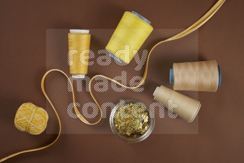 A yellow collection of sewing and tailoring tools arranged on a brown background