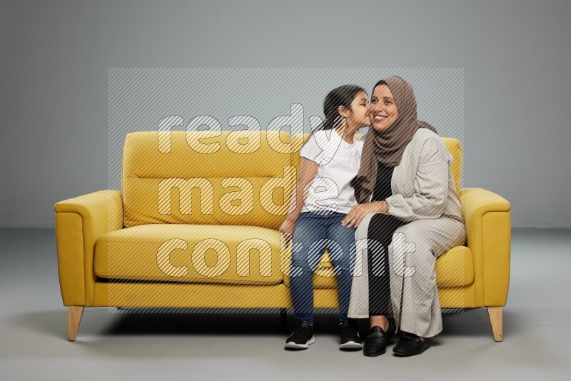 A girl with her mother sitting and interacting with the camera on gray background