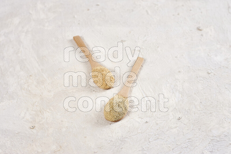 Two wooden spoons full of ground ginger powder on white background