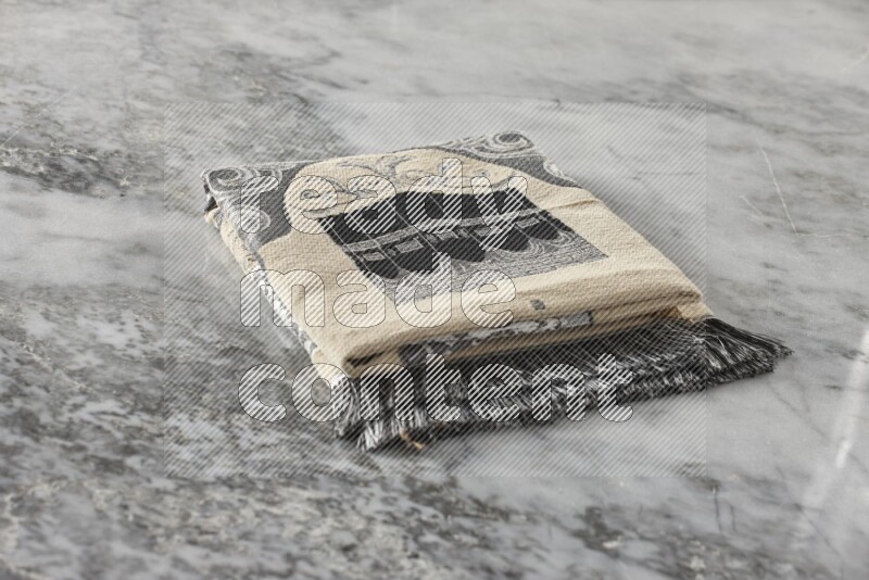 A folded prayer mat with different elements such as quran and prayer beads on grey marble background