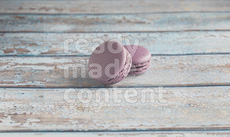 45º Shot of two Purple Blueberry macarons on light blue wooden background