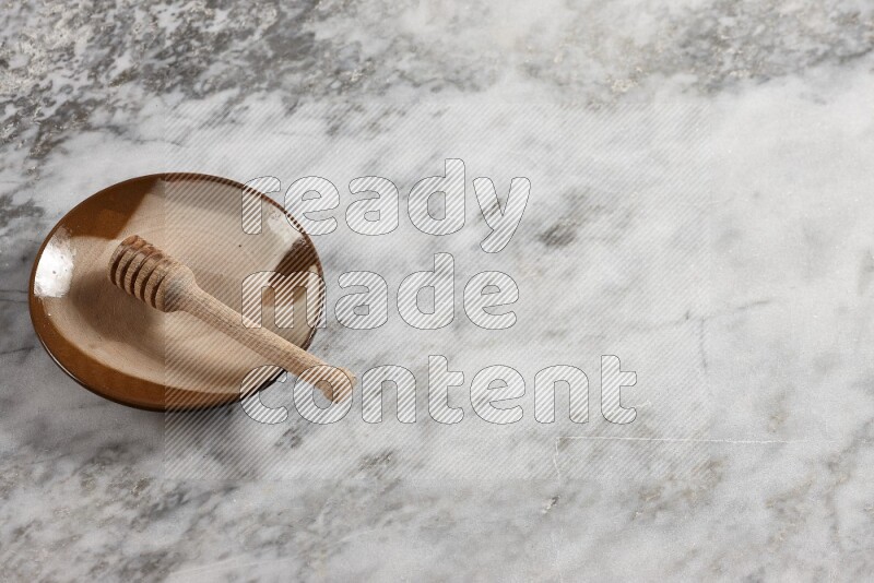Multicolored pottery plate with wooden honey dipper in it on grey marble background